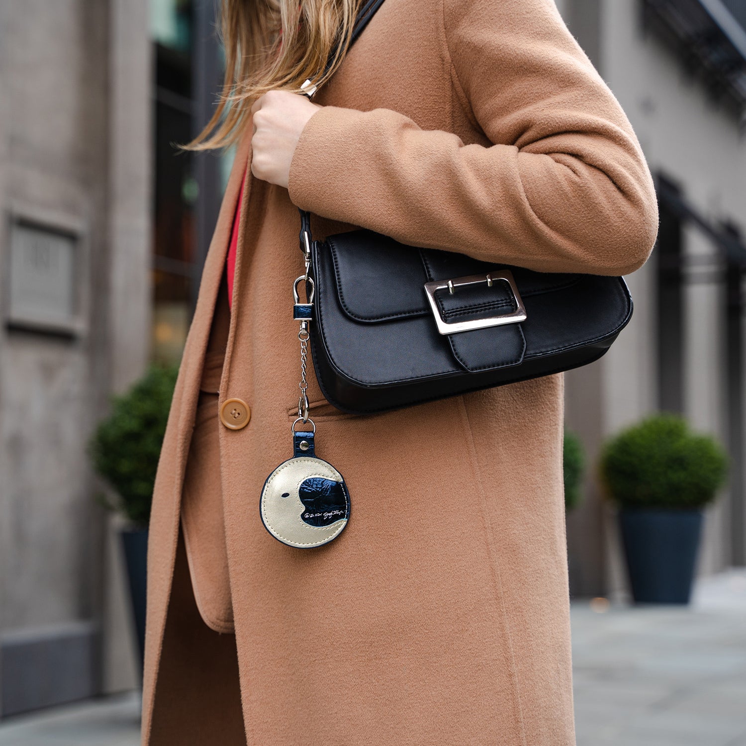 Woman walking downtown wearing a wool coat and holding a leather purse with The Keeper Moon AirTag holder in leather